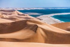 Golden Sand Dunes Meet Turquoise Ocean Dramatic aerial view of massive golden sand dunes adjacent to a pristine turquoise ocean and white