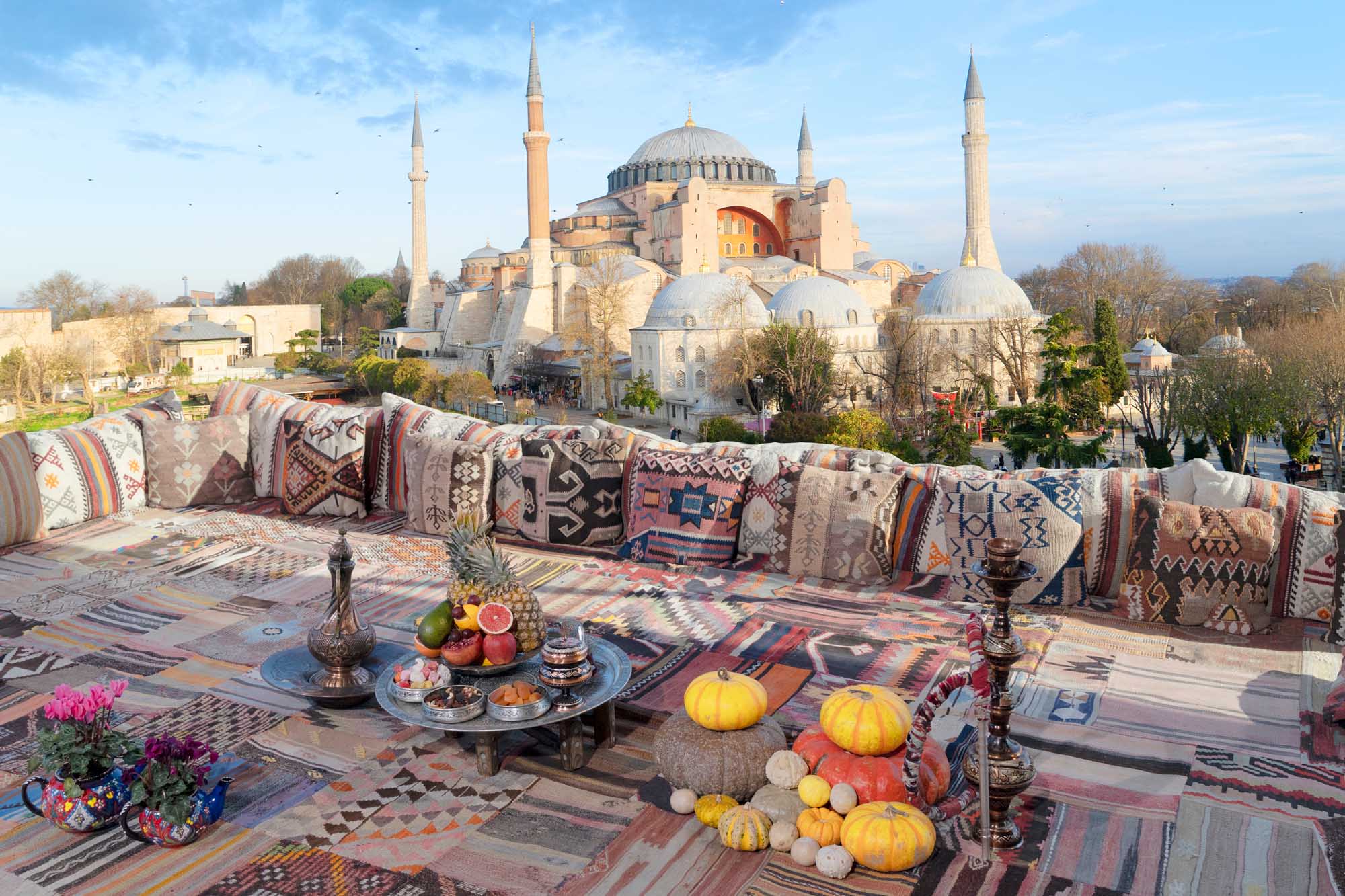 A stunning rooftop terrace featuring traditional Turkish cushions, kilim textiles, and autumn produce overlooking the iconic Hagia Sophia mosque in Istanbul, Turkey.