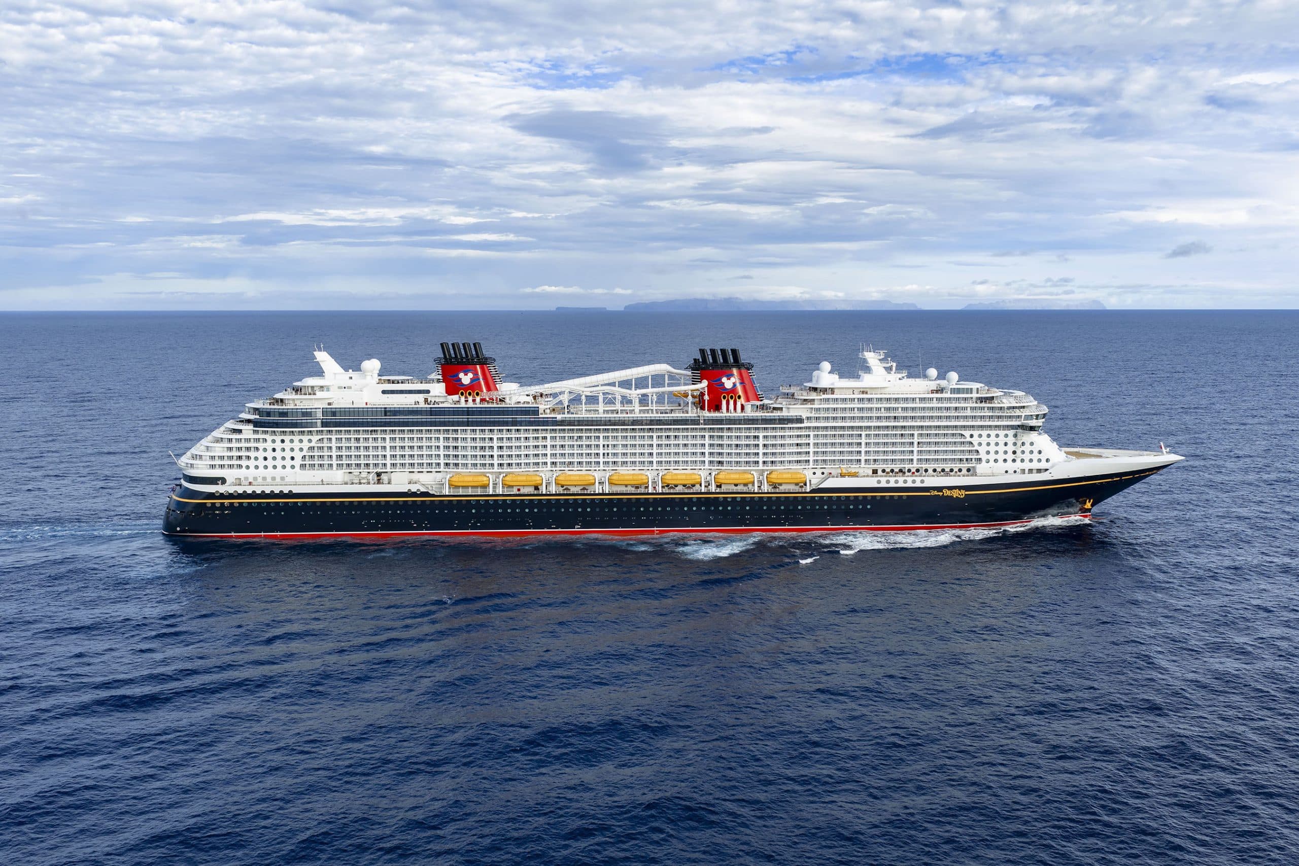 Large Cruise Ship at Sea with Mountains A large Disney cruise ship at sea with mountains in the background under clear skies.