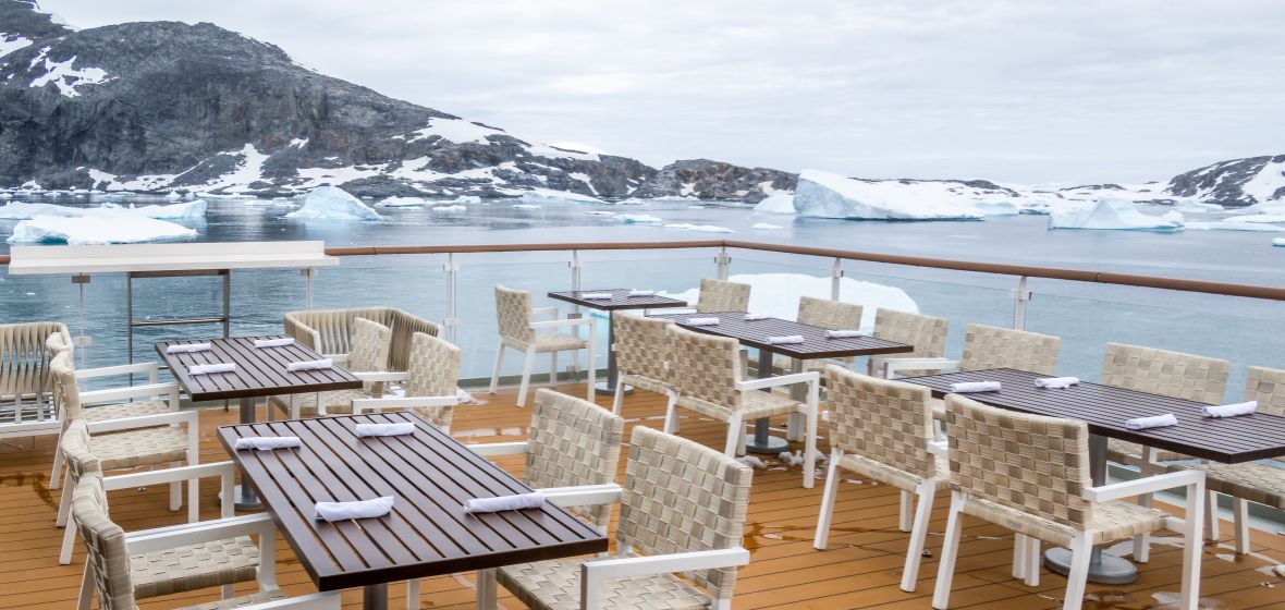 Luxury Dining Deck with Arctic Glacier Views An elegant outdoor dining and lounge area aboard a cruise ship overlooking a pristine Arctic