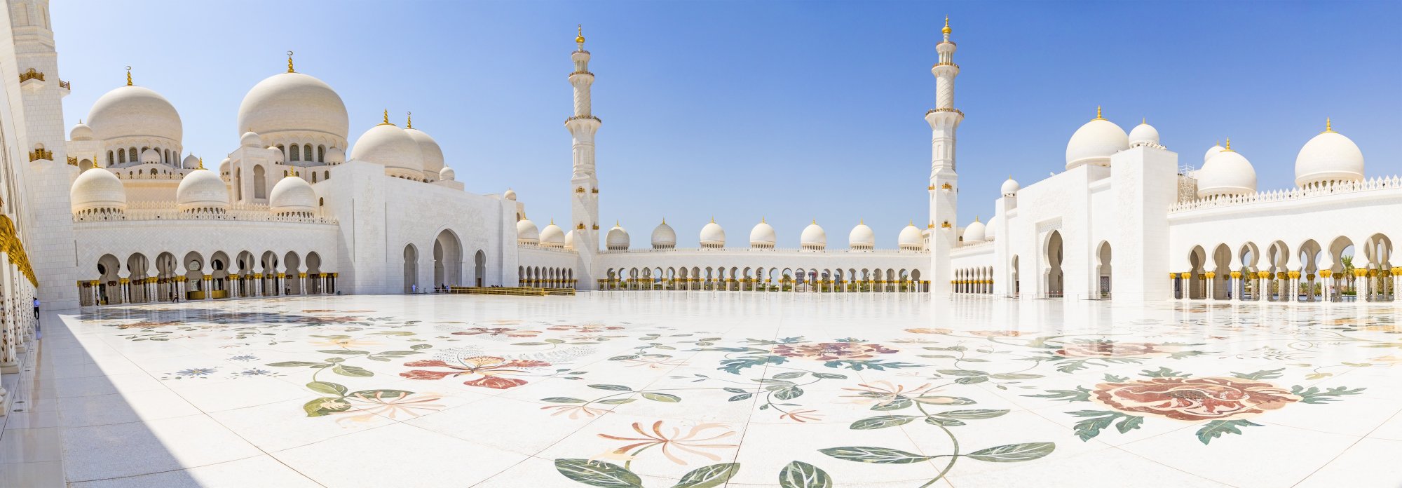 A stunning view of the Sheikh Zayed Grand Mosque in Abu Dhabi, featuring its iconic white marble architecture with golden domes and minarets, ornate floral marble inlay patterns covering the vast courtyard floor.