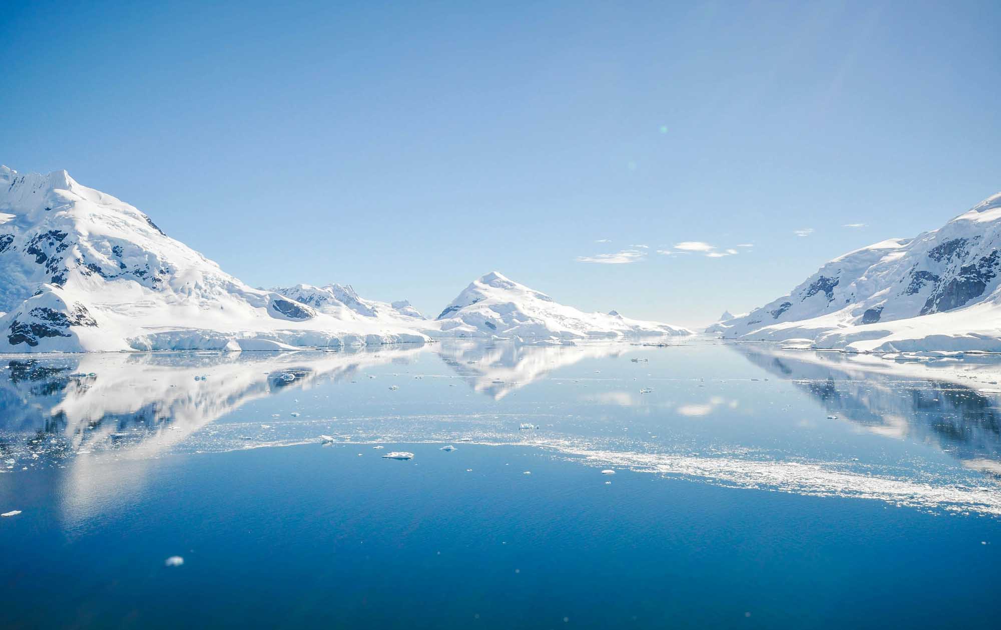 Snow-Capped Mountains and Icebergs in Antarctic Waters A breathtaking Arctic or Antarctic landscape featuring pristine snow-covered mountains reflected in calm, clear waters dotted with icebergs.