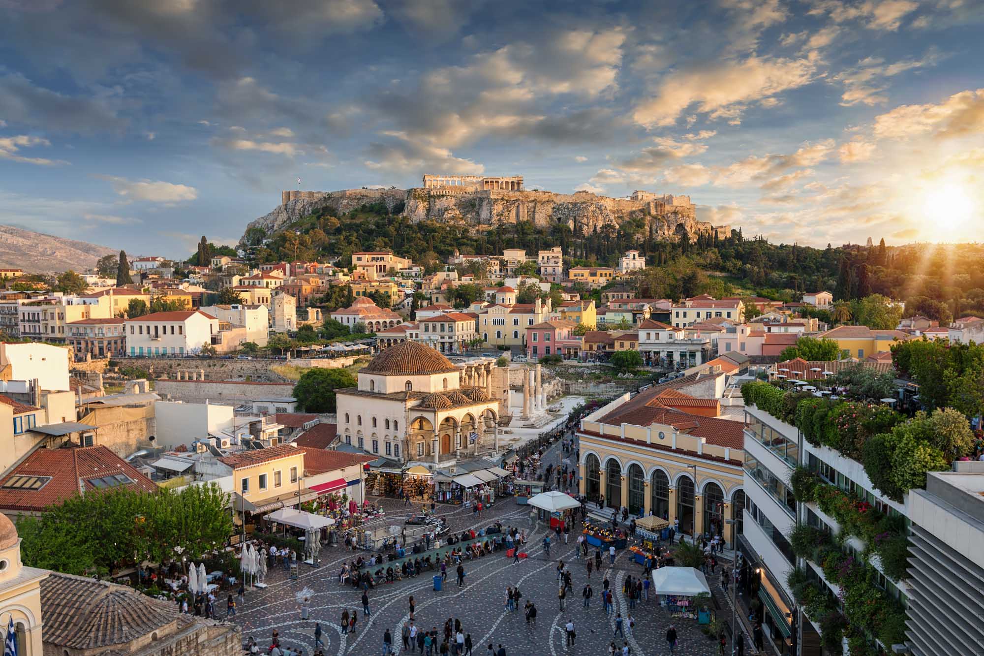 Sunset Over Plaka with Acropolis, Athens A stunning golden-hour view of Athens' historic Plaka district with colorful neoclassical buildings clustered below the illuminated Acropolis and Parthenon Temple perched atop a rocky hill.