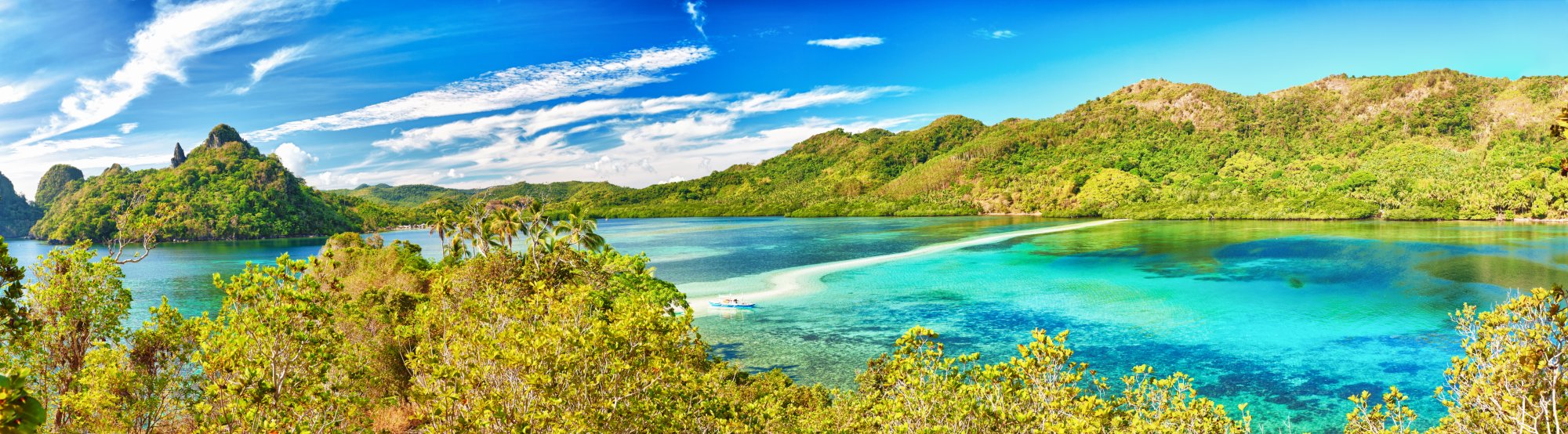 Tropical Island Lagoon with Limestone Cliffs A stunning aerial view of a pristine tropical lagoon featuring crystal-clear turquoise waters, white sand beaches, lush green mangrove forests, and dramatic limestone cliffs under a bright blue sky. The scenic landscape captures the natural beauty of a remote island destination ideal for cruise tourism and water activities.
