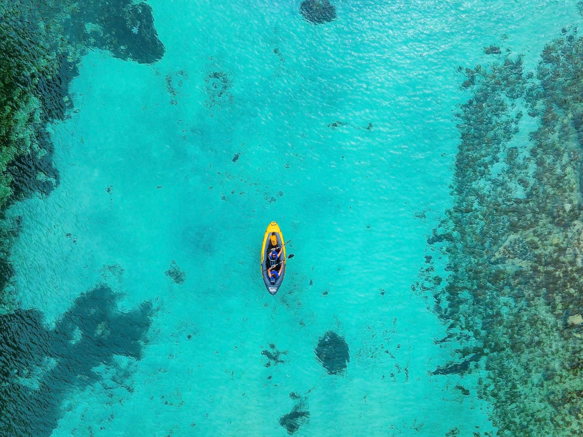 An aerial view of a solo kayaker in a bright yellow kayak navigating crystal-clear turquoise waters