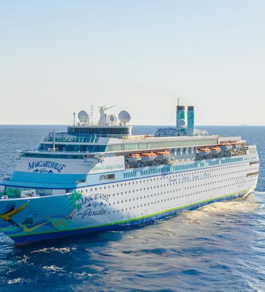 Margaritaville at Sea Cruise Ships Docked Two large cruise ships are docked side by side in calm blue ocean waters. The foreground vessel