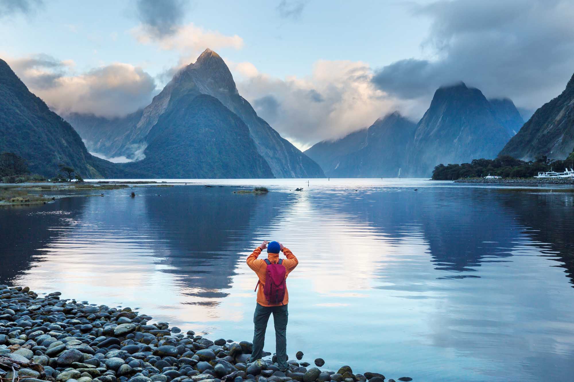 A solo hiker in vibrant outdoor gear stands on a rocky shore, gazing across the pristine waters